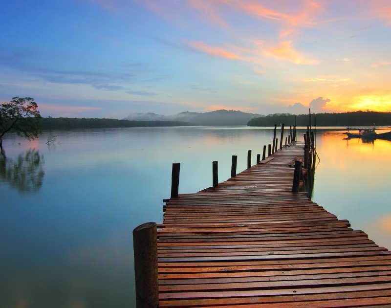 A dock leading into a lake during sunrise.