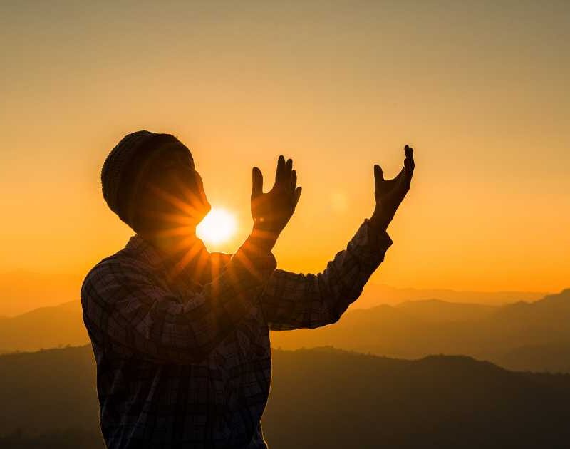 Man standing with praying hands outstretched at sunrise.