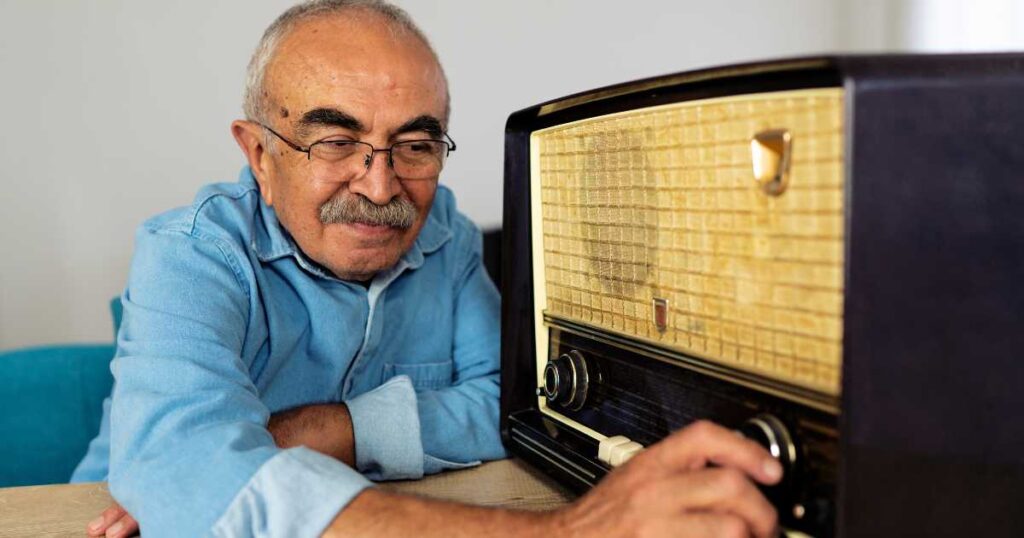Older man with glasses adjusting the knobs on a retro styled radio.