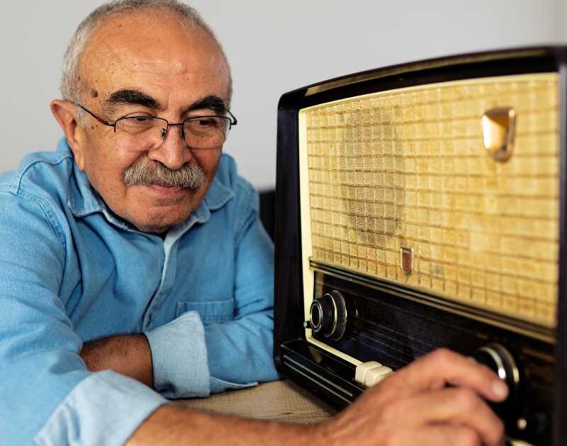 Older man with glasses adjusting the knobs on a retro styled radio.