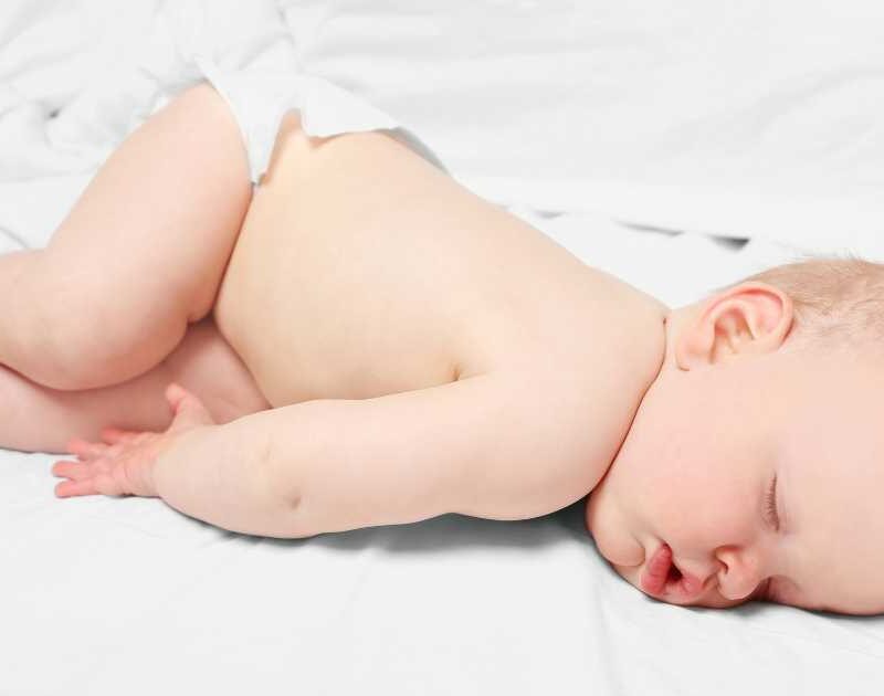 Sleeping baby in a diaper on a white sheet.