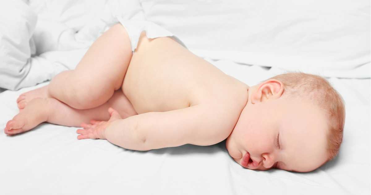 Sleeping baby in a diaper on a white sheet.