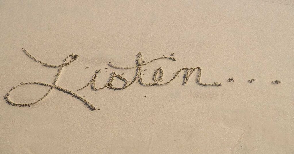 The word "listen" written in the sand in cursive with three dots following.